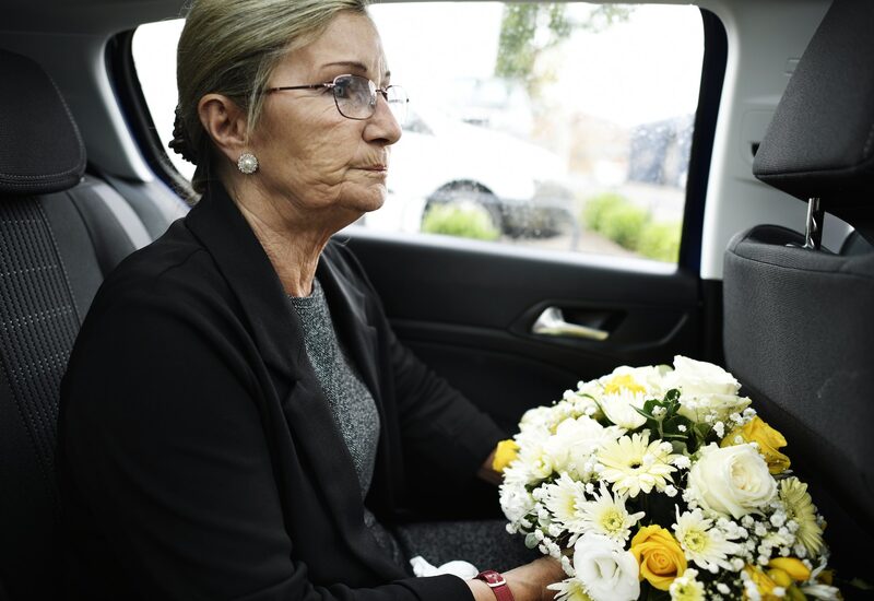 A woman holding flowers in the back of a car on the way to a funeral